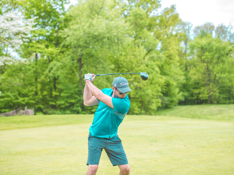 man dressed in blue golfing on a beautiful, lush, green golf course with vivid green trees in the background.