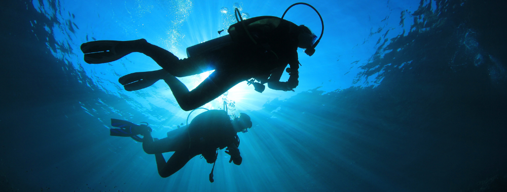 2 scuba divers in the water with the light above them